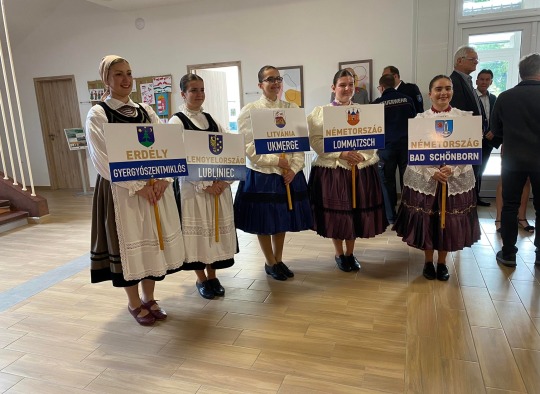 Tautiniais kostiumais vilkinčios moterys su delegacijų iš miestų-partnesių lentelėmis